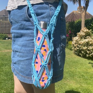 May include: A blue crocheted water bottle holder with a pink and yellow patterned water bottle inside. The holder is worn around the waist.