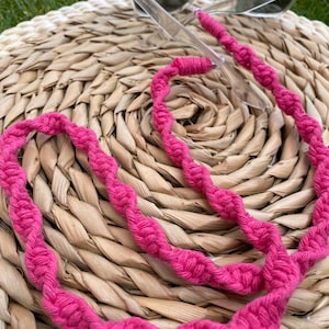 Peut inclure: Un cordon tressé rose pour lunettes. Le cordon est fait d'un fil épais et torsadé et est conçu pour maintenir les lunettes en sécurité autour du cou.