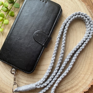 May include: A black leather phone case with a gray braided phone strap. The strap has a black plastic clip.
