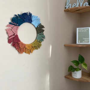 Puede incluir: Un tapiz de macram&eacute; de pared colorido con forma circular y flecos. El tapiz est&aacute; hecho con diferentes tonos de rosa, rojo, naranja, amarillo, verde, azul y azul marino.