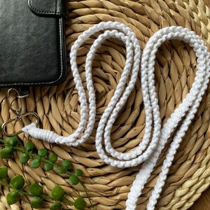 May include: White cotton cord phone strap with a silver clasp. The strap is coiled on a woven straw mat.