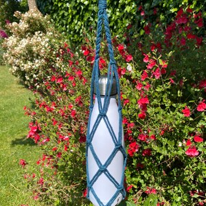 May include: A teal blue crocheted bottle holder with a white water bottle inside. The holder is hanging from a silver carabiner.