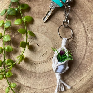May include: A white macrame plant hanger with a small potted plant and a green plastic key chain attached to a silver key ring.