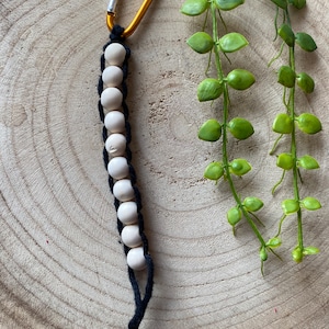 May include: A white wooden bead keychain with a black cord and a gold carabiner clip.