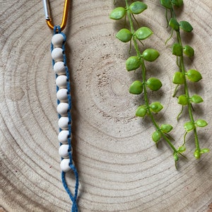 May include: A white wooden bead keychain with a gold carabiner clip and blue string. The keychain is on a wooden surface.