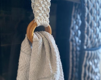 Pode incluir: Um anel de toalha de crochê branco com um anel de madeira pendurado em uma alça de forno prateada. Uma toalha cinza está pendurada no anel.