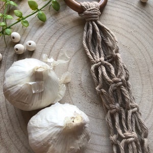 May include: A wooden ring with a macrame plant hanger made of natural beige rope. Two white garlic bulbs are on a wooden surface.