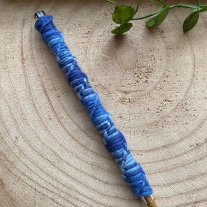 May include: A blue and white yarn-wrapped pencil on a wooden surface.