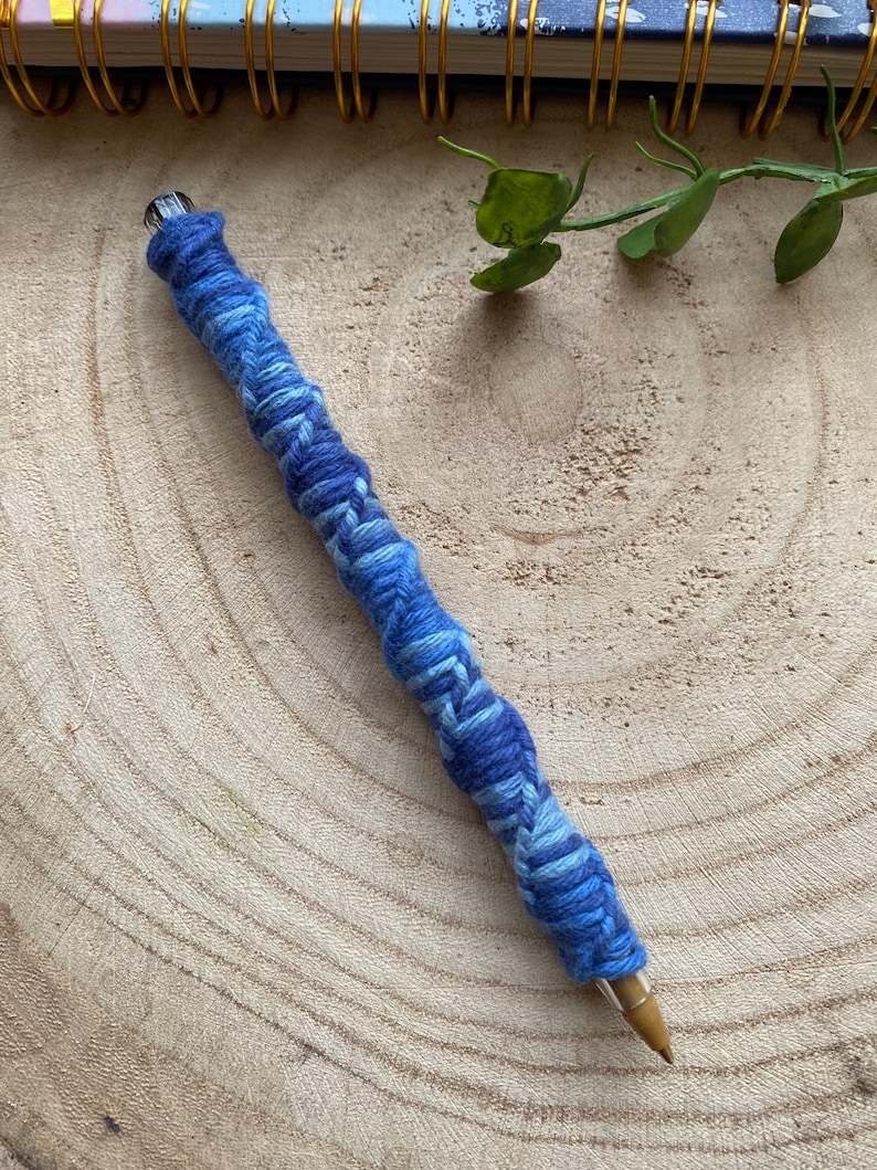 May include: A blue and white yarn-wrapped pencil on a wooden surface.