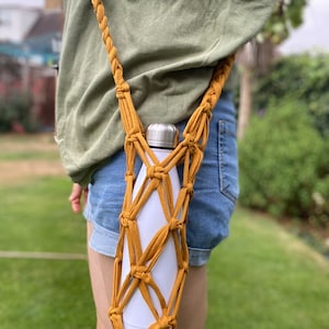 May include: A mustard yellow crocheted water bottle holder with a white water bottle inside. The holder is worn as a crossbody bag.