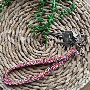 May include: A colorful braided key chain with a pink, orange, and white pattern. The keychain is attached to a set of keys.