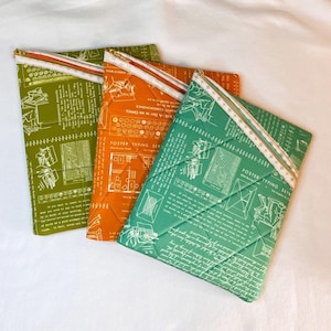 May include: Three quilted fabric cases in green, orange, and teal, each with a white and gold zipper. The cases feature a vintage typewriter schematic print. The cases are designed with a diagonal quilted pattern.