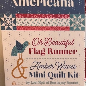 May include: A quilt kit featuring a red, white, and blue Americana theme. The kit includes a flag runner and a mini quilt. The text on the packaging reads "Oh Beautiful Flag Runner & Amber Waves Mini Quilt Kit by Lori Holt of Bee in my Bonnet".