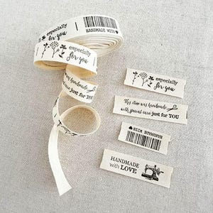 May include: A roll of off-white fabric ribbon and four individual rectangular fabric labels printed with black ink. The designs include floral motifs, a barcode, a sewing machine icon, and text reading especially for you, handmade with love.