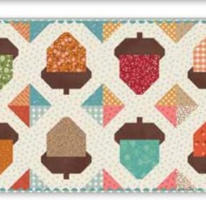 May include: A rectangular quilt featuring a repeating pattern of eight stylized acorns arranged in two rows. Each acorn has a dark brown cap and a uniquely patterned body in shades of green, orange, red, and teal, set against a cream background.