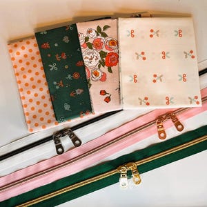 May include: Four rectangular fabric swatches featuring orange polka dots, dark green floral patterns, pink rose prints, and white with small red and blue flower motifs, paired with three long zippers in white, pink, and dark green with metal pulls.