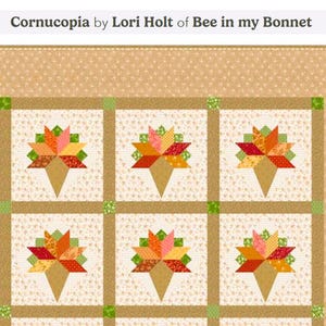 May include: A quilt featuring the Cornucopia by Lori Holt of Bee in my Bonnet pattern. The design consists of six blocks with cornucopia motifs in shades of orange, red, yellow, and green, set against a cream background with a tan border.