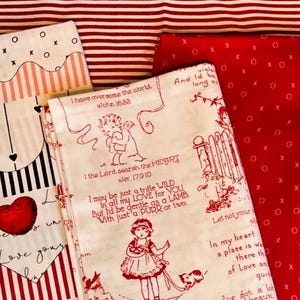 May include: Assortment of Valentine's Day themed fabric pieces. Designs include red hearts, black and white stripes, and text. One fabric has a large red heart and the words "loved love yours". Another has a drawing of a girl and a dog.