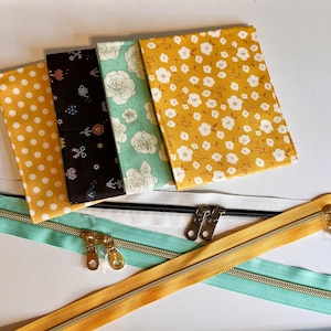 May include: An assortment of fabric pieces with various patterns, including polka dots, floral, and botanical designs. Zippers in teal, white, and yellow with gold-colored metal zipper pulls are also visible. These items are likely for sewing or crafting projects.