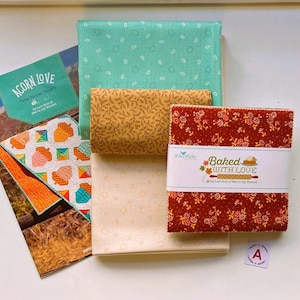 May include: A quilting fabric bundle featuring a pattern booklet titled Acorn Love, a stack of folded fabric in teal, mustard yellow, and cream, and a square stack of red floral fabric with a band labeled Baked With Love by Riley Blake.