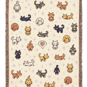 May include: Cream-colored woven throw blanket featuring a repeating pattern of pixelated cats in various poses and colors, including brown, black, and yellow. The blanket has a fringed edge and small purple star accents.