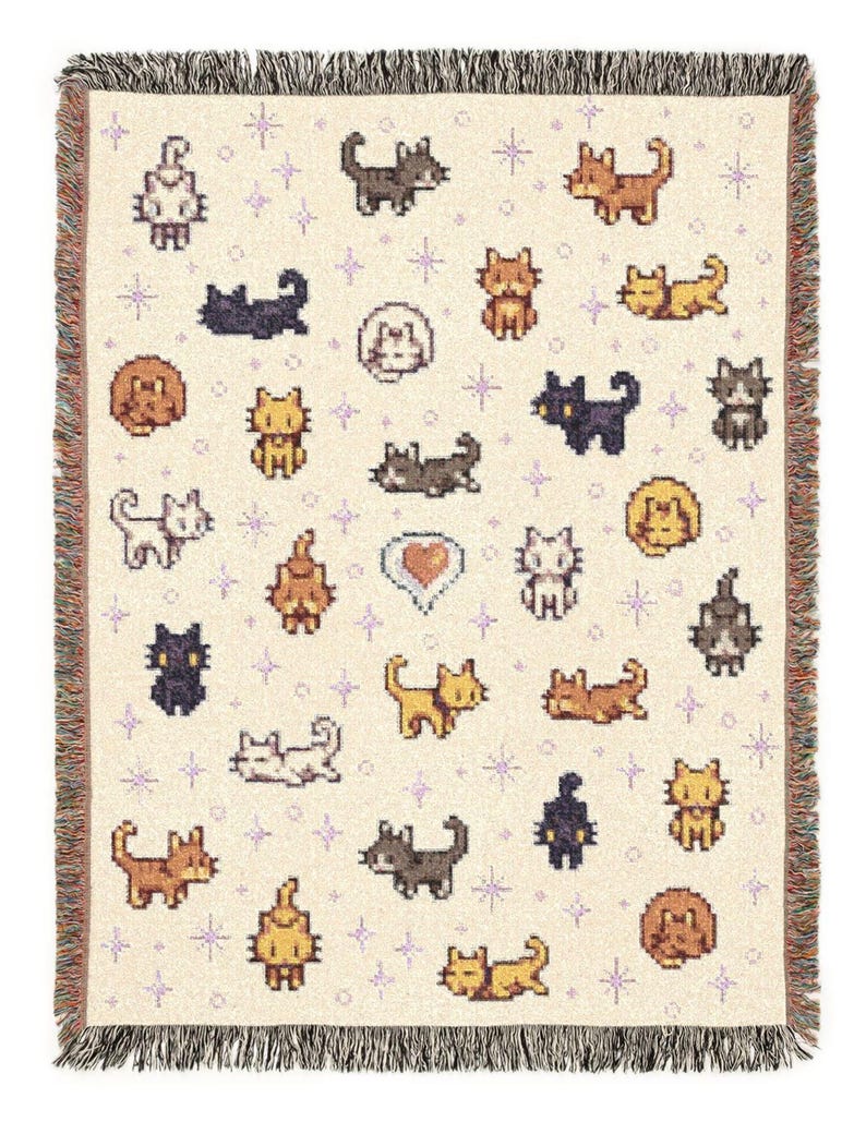 May include: Cream-colored woven throw blanket featuring a repeating pattern of pixelated cats in various poses and colors, including brown, black, and yellow. The blanket has a fringed edge and small purple star accents.