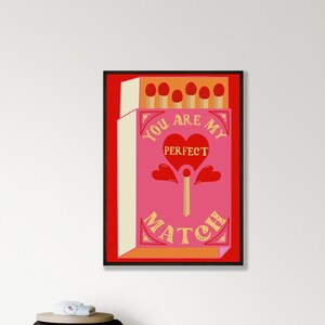 Op de afbeelding: Een rode en roze luciferdoos met de tekst "You are my perfect match" in gele letters. De luciferdoos heeft een rood hart met het woord "perfect" erin en een enkele lucifer met een rood hart bovenaan.
