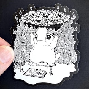 May include: A black and white illustration of a platypus performing a ritual. The platypus is standing on a book with a pentagram symbol. There are candles on either side of the book. The platypus is surrounded by flames and a pentagram symbol is above its head.