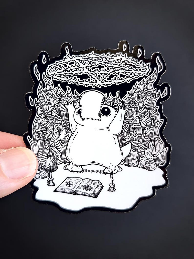 May include: A black and white illustration of a cartoon platypus performing a ritual with a pentagram, candles, and a book with a pentagram on the cover. The platypus is surrounded by flames.
