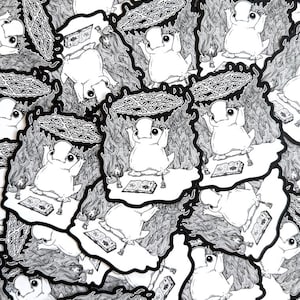 May include: A stack of black and white stickers featuring a cartoon frog character performing a ritual with a pentagram and books. The frog is wearing a crown and has a surprised expression.