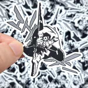 May include: Black and white sticker featuring a stylized robot head with sharp angles and details. The design includes graphic elements and is held against a background of similar stickers.