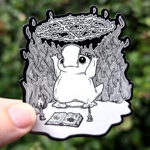 May include: Black and white illustration of a cartoon frog holding a pentagram above its head. The frog is standing on a book with a pentagram on the cover. There are candles on either side of the book.