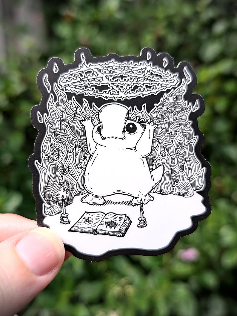 May include: A black and white illustration of a platypus performing a magic trick. The platypus is standing on a book with a pentagram symbol and surrounded by flames. Above the platypus is a swirling cloud of smoke.