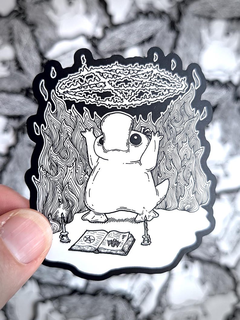 May include: A black and white illustration of a cartoon platypus performing a ritual. The platypus is standing on a book with a pentagram symbol and two candles. A circle of fire surrounds the platypus and a cloud of smoke is above its head.