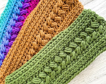 May include: Four crocheted headbands in different colours: blue, purple, brown, and green. The headbands are stacked on top of each other, with the green headband at the bottom. The headbands are made with a textured stitch.