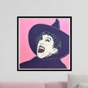 Könnte beinhalten: Ein gerahmter Druck einer Frau, die einen schwarzen Hexenhut und eine lila Robe trägt und lachend den Mund aufmacht. Der Hintergrund ist rosa.