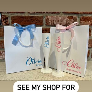 May include: Two white gift bags with blue and pink ribbons. The bags are decorated with the names "Olivia Bride" and "Chloe Bridesmaid".