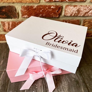 May include: Two white gift boxes with pink ribbon bows. The top box has the name "Olivia Bridesmaid" printed on it in brown lettering.