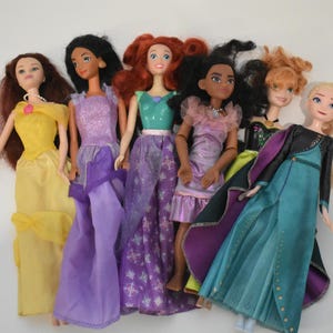 May include: A collection of seven dolls, each dressed in colorful gowns. The dolls have various hair colors, including red, black, and blonde. The dresses are in shades of yellow, purple, green, and blue.