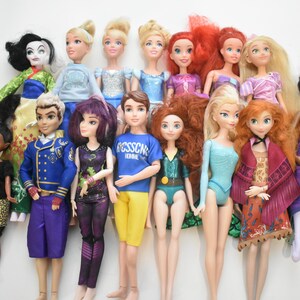 May include: A collection of fashion dolls with various hairstyles and outfits. The dolls feature a range of skin tones and are dressed in colorful clothing, including dresses, tops, and pants. Some dolls have long hair, while others have shorter styles.