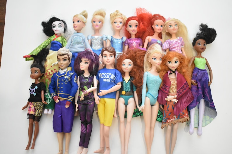 May include: A collection of fashion dolls with various hairstyles and outfits. The dolls feature a range of skin tones and are dressed in colorful clothing, including dresses, tops, and pants. Some dolls have long hair, while others have shorter styles.