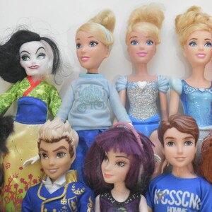 May include: A collection of dolls featuring various characters. The dolls have different hair colors and styles, and are wearing a variety of outfits. The dolls are arranged in a group, with some standing in the front and others in the back.