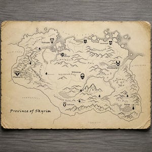 May include: A rectangular map of the Province of Skyrim printed on aged, tan-colored paper with deckled edges. The map features black line drawings of mountain ranges, rivers, and regional labels, along with various city icons and the text Province of Skyrim.