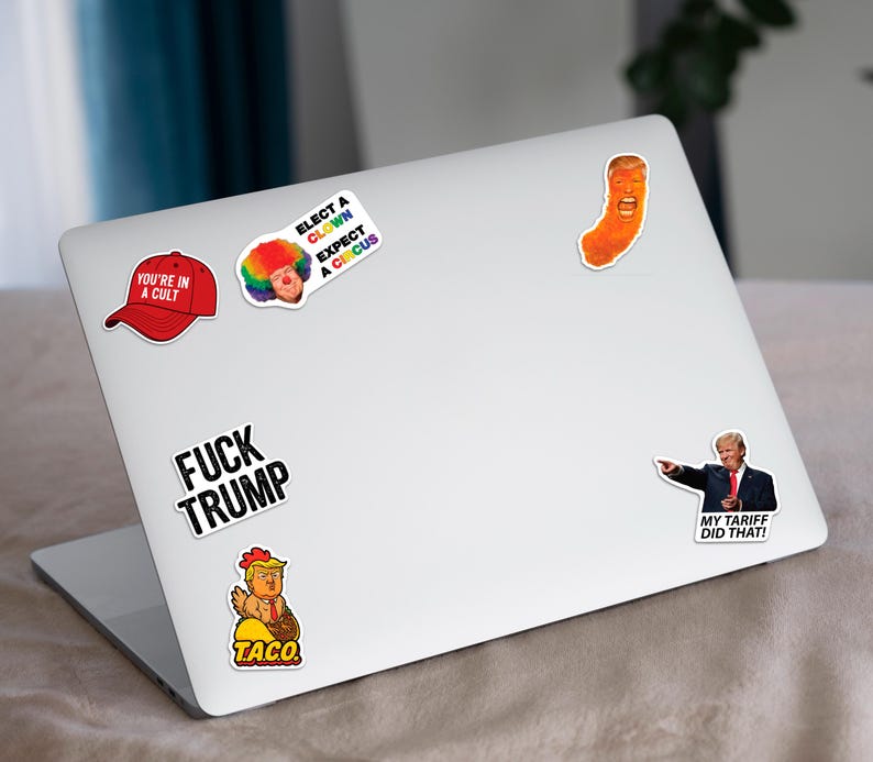 May include: A laptop covered in political stickers. Stickers include a red baseball cap with "YOU'RE IN A CULT", a clown with "ELECT A CLOWN EXPECT A CIRCUS", and a cartoon of Trump as a Cheeto. Other stickers say "FUCK TRUMP" and "MY TARIFF DID THAT!"
