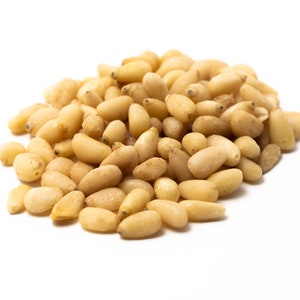 Könnte beinhalten: Nahaufnahme eines Haufens hellbrauner Pinienkerne auf weißem Hintergrund.