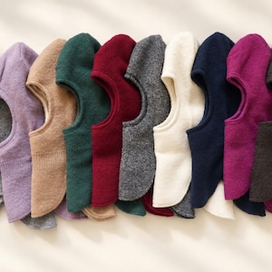 May include: A collection of ten balaclavas arranged in a row, featuring a variety of solid colors including gray, lavender, tan, dark green, burgundy, charcoal, cream, navy blue, magenta, and dark brown, all with a ribbed neck detail.