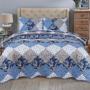 May include: A blue and grey floral patterned quilt with a scalloped edge. The quilt is on a bed with two matching pillowcases.