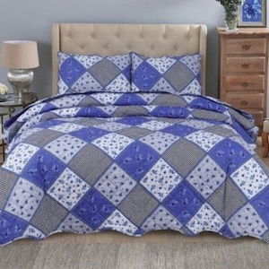 May include: A blue and white patchwork quilt with a floral pattern. The quilt is on a bed with white pillowcases and a white headboard.