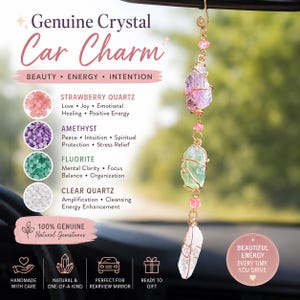 May include: A car charm featuring three raw, wire-wrapped crystals hanging from a gold-toned metal hook. The stones include a pink strawberry quartz, a green fluorite, and a clear quartz, accented with small pink beads and gold wire links.