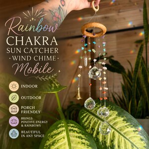 May include: A sun catcher wind chime mobile featuring a circular wooden frame with hanging strands of multi-colored gemstone beads, clear crystal prisms, and a small gold-toned metal bell. Text on the image reads Rainbow CHAKRA SUN CATCHER.